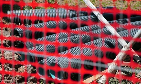 Road yard with conduits and the red safety mesh of the site prot — Stock Fotó