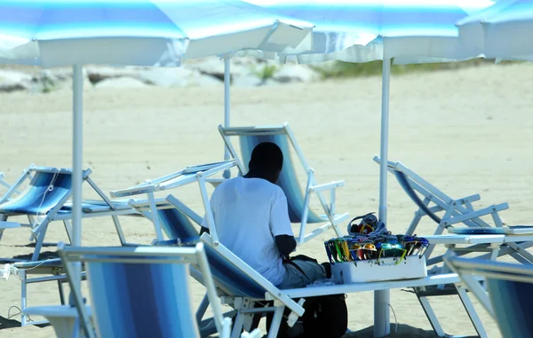Vendedor africano descansará bajo sombrilla en la playa en verano —  Fotos de Stock