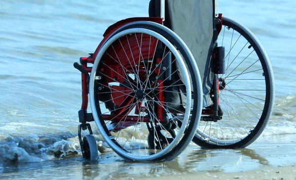 Silla de ruedas-rojo por el mar en la playa de arena en verano — Foto de Stock