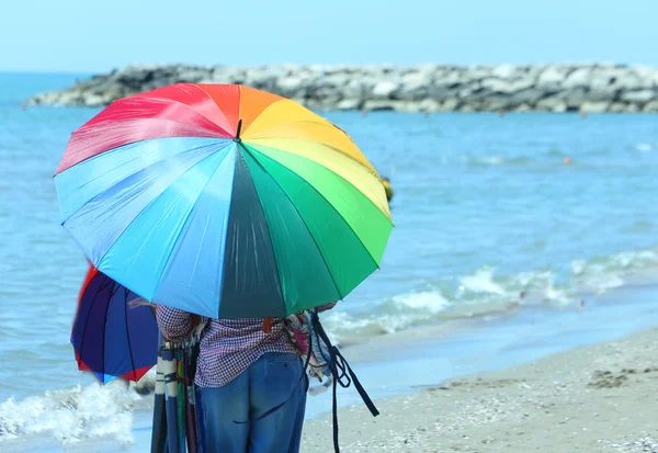 Elder vendedor ambulante de sombrillas de colores junto al mar en la playa en s — Foto de Stock