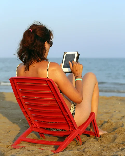 Opalony kobieta czyta ebook na plaży — Zdjęcie stockowe