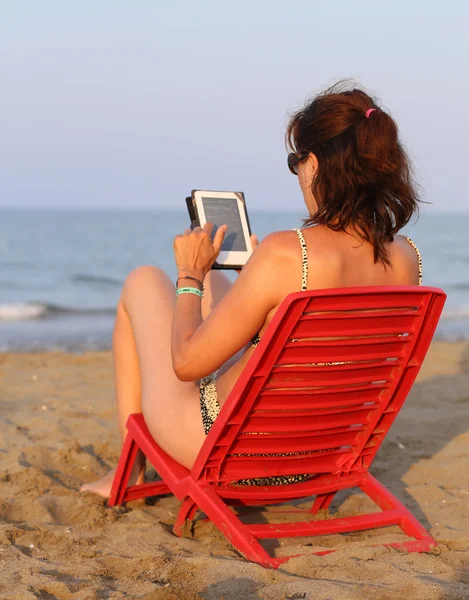 Tanned woman reads the ebook on the seashore i — Stock Photo, Image