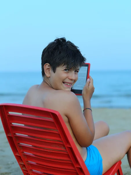 Sourire garçon lit l'ebook sur la plage — Photo