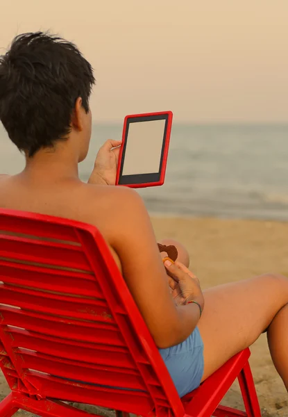 Giovane ragazzo legge l'ebook sulla spiaggia — Foto Stock