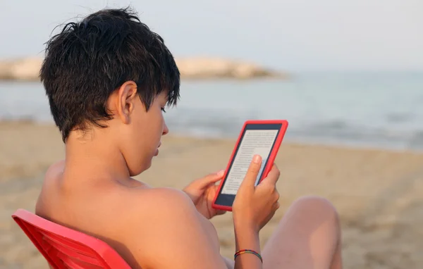 Young boy reads the ebook on the sea shore in summer — Stock Photo, Image