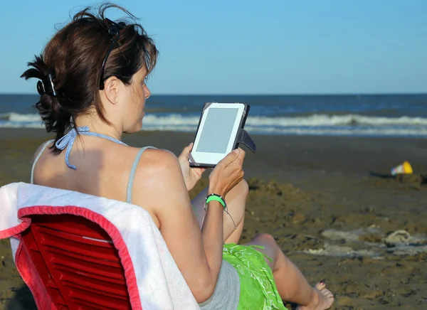 日焼けした女性が海岸で電子ブックを読み取ります — ストック写真