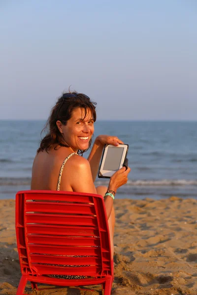 Piękna kobieta uśmiechający się czyta ebook na plaży — Zdjęcie stockowe