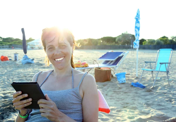 Beautiful smiling woman reads the ebook on the beach — Stock Photo, Image