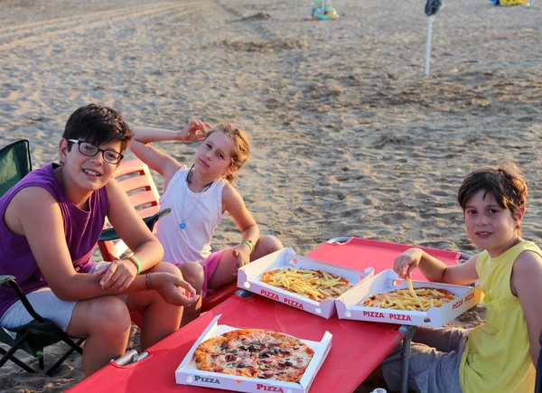 Happy three brothers eating pizza on the beach — Stock Photo, Image