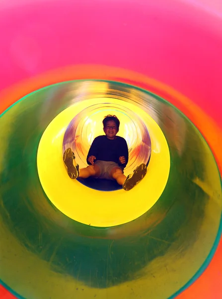 Happy child slides in multicolored tunnel slide in the playgroun — Stock Photo, Image