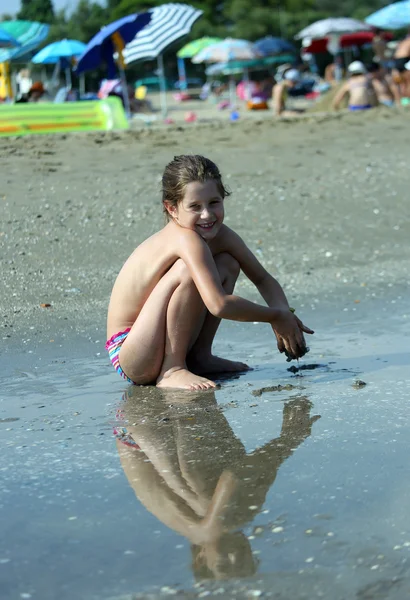Маленькая девочка в купальнике приседает на пляже — стоковое фото