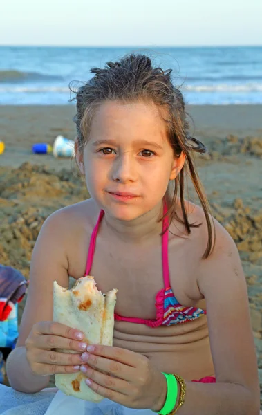 Mała dziewczynka jedzenie smaczne flatbread na brzegu plaży i — Zdjęcie stockowe