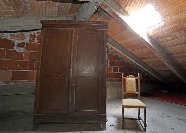 Wooden wardrobe and an antique chair in the dusty attic — Stock Photo, Image