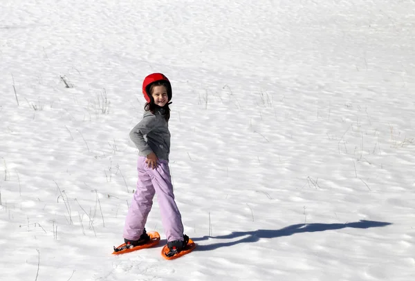 Niña sonriente con casco y raquetas de nieve en la nieve —  Fotos de Stock