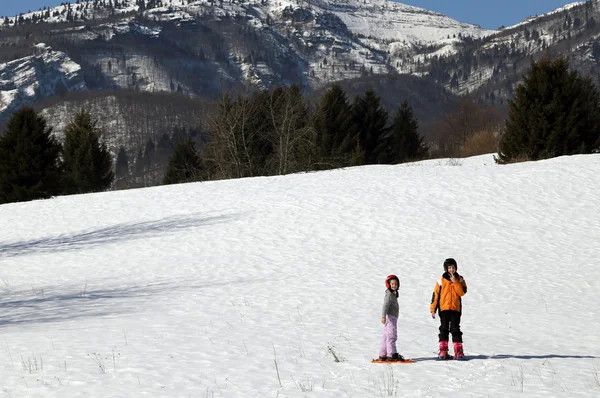 Duas crianças com capacete e sapatos de neve na neve — Fotografia de Stock