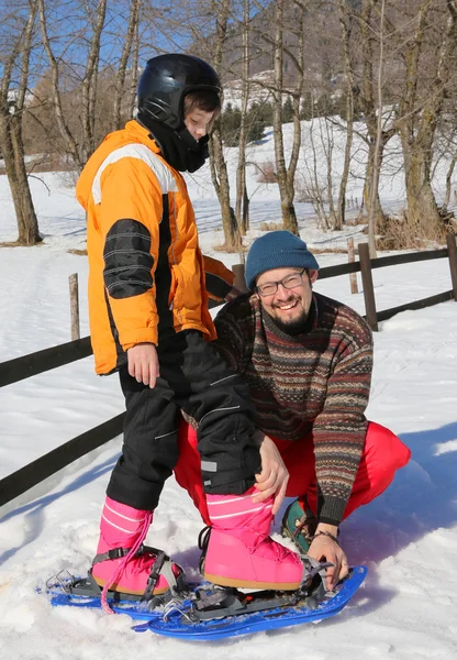 Uśmiechnięty ojciec pomoc syna do noszenia rakiety śnieżne — Zdjęcie stockowe