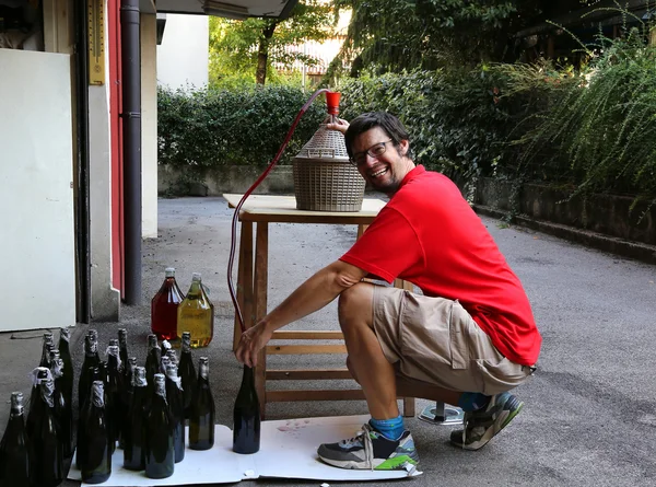 Young man smiling while bottling the wine at home — Stock Photo, Image