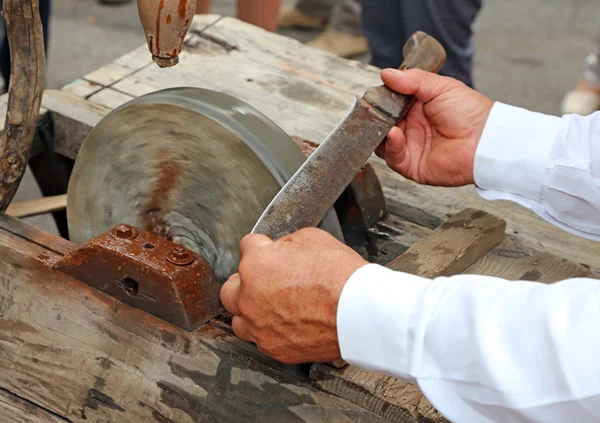 Anciano mientras afilaba la hoja del cuchillo en la rueda de agua — Foto de Stock