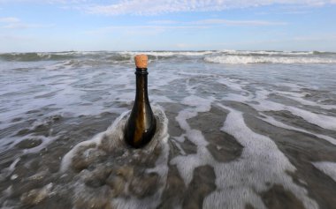 Okyanus gelgitinin üzerinde mantar tıpası olan siyah cam şişe içinde gizli bir mesaj tutuyor.