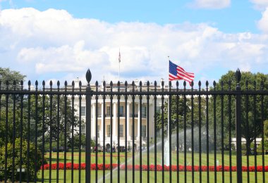 Washington, DC, ABD - 26 Ağustos 2025: Amerikan bayrağı sallama ve arka planda Beyaz Saray yüksek demir korumalı korkulukların arkasında