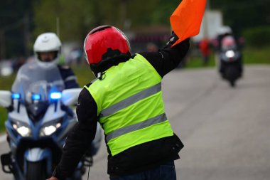 Spor yarışında polis motosikletinin yanında floresan güvenlik yeleği giymiş bir trafik polisi.