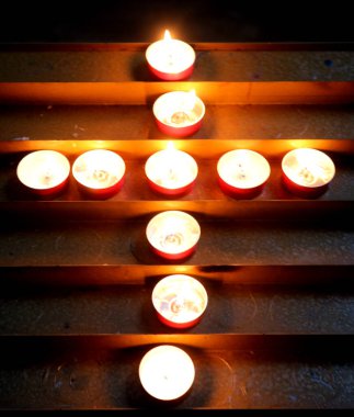 Kasvetli ibadet mekânında kutsal bir haç sembolü oluşturan bir sürü küçük mum var.