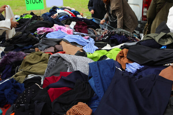 Heap of many assorted second hand apparel dresses and clothes dumped on a used goods stand