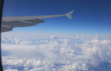 Beyaz bulutlar ve mavi gökyüzü üzerinde uçan bir jet uçağının kanadı.