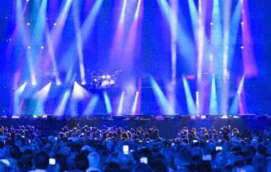 Geniş sahnedeki stadyumda insanlar konser veriyor ve bir sürü ışık yanıyor.