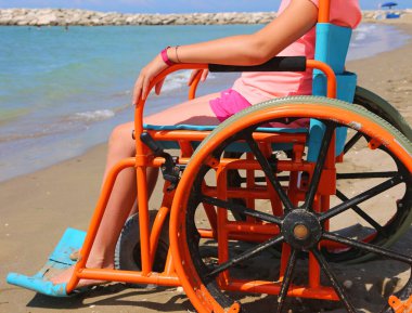 Tekerlekli sandalyesi deniz kıyısında hareket etmesi için modifiye edilmiş küçük bir kız.