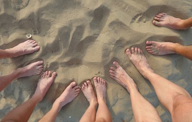Kumsalda birlikte duran farklı insanlara ait çıplak ayakların yakın görüntüsü.