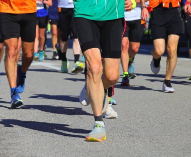 Koşu ayakkabıları ve bacakları da spor tozluklarıyla birçok erkek ve kadın amatör ve profesyonel olmayan koşucular asfalt sokaktaki yol yarışı şehrinde