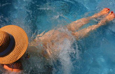 Bacakları genç, beyaz kadın jakuziyi rahatlatırken geniş hasır şapka giyiyor.