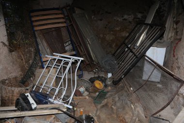 Eski sandalyelerle dolu dağınık ve terk edilmiş bir bodrum tablosu ve karanlık, kirli ve bakımsız bir ortamda atılmış mobilya parçaları.