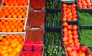 Kırmızı domates, yeşil kabak ve olgun portakalların yer aldığı tezgahta satılık bir sürü meyve var.