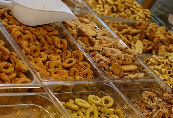 Beyaz kepçeyle cam bir kutuda sergilenen farklı şekilli ve desenli İtalyan tuzlu kraker veya tarallini çeşitlerinin yakın plan görüntüsü