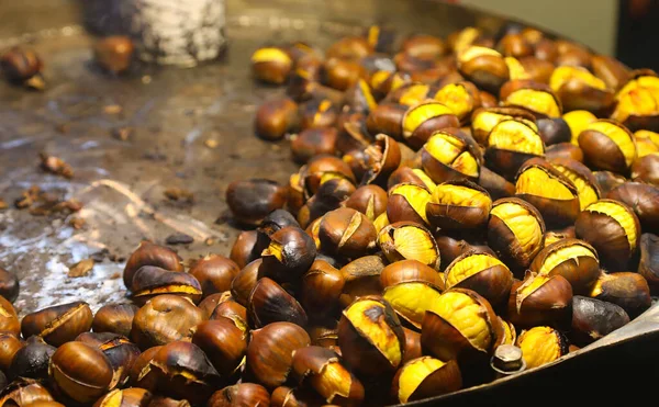 Yakın çekim, kavrulmuş kestaneler, parlak kahverengi deniz kabukları, koyu yüzeyde metal tepsi.