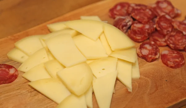 Cutting board with cheese and salami slices — Stock Photo, Image