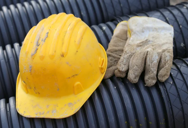 Желтая шляпа и рабочие перчатки на строительной площадке — стоковое фото