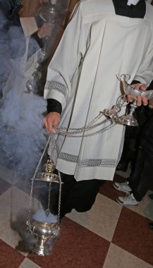 Priest in cassock blesses the faithful with incense during Mass clipart
