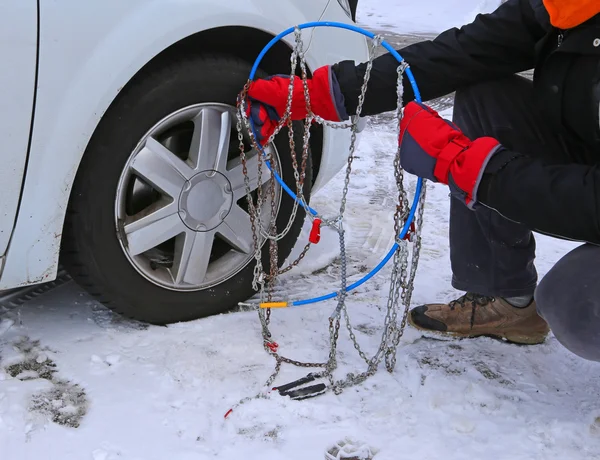 Homem com luvas vermelhas instalar correntes de neve no pneu do carro na neve — Fotografia de Stock
