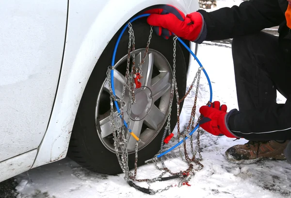 Hombre con guantes rojos instalar cadenas de nieve en el neumático del coche — Foto de Stock