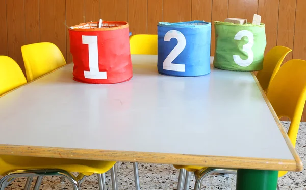 Escrivaninha de um quarto de crianças com jarros numerados e pequenas cadeiras amarelas — Fotografia de Stock