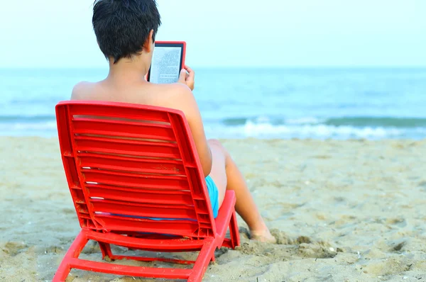 Mladý chlapec čtení ebook na červené židle — Stock fotografie