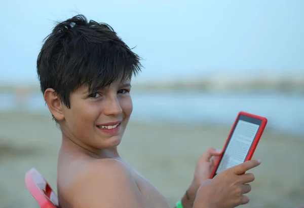 Garçon avec cheveux noirs lit un ebook sur la plage à la mer — Photo