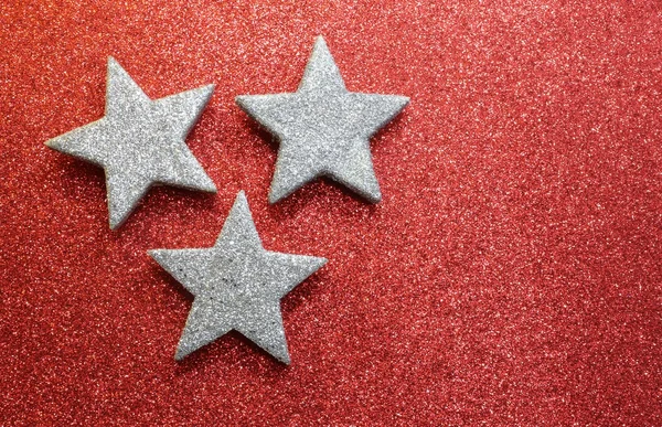 Drie zilveren sterren op heldere rode glittery textuur — Stockfoto