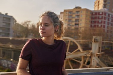 Korkuluklara yaslanan ve mesafeye bakan genç bir kadın.