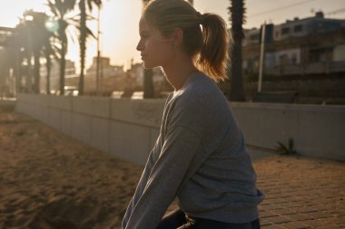 Genç bir kadın okyanusa bakarken kaldırıma oturur.