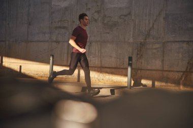 Eşofman giymiş genç adam büyük bir beton duvarın önünden geçiyor.