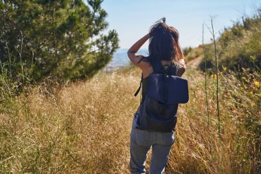 Havalı genç bir bayan ellerini saçlarında gezdirirken doğada yürüyor.